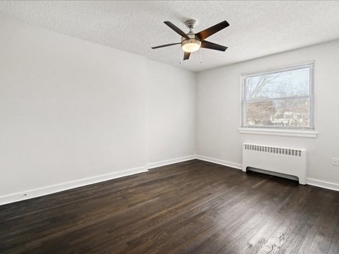 A room with a ceiling fan and a window with a view of a residential area.