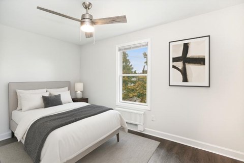 A bedroom with a bed, a ceiling fan, and a window with a view of trees.
