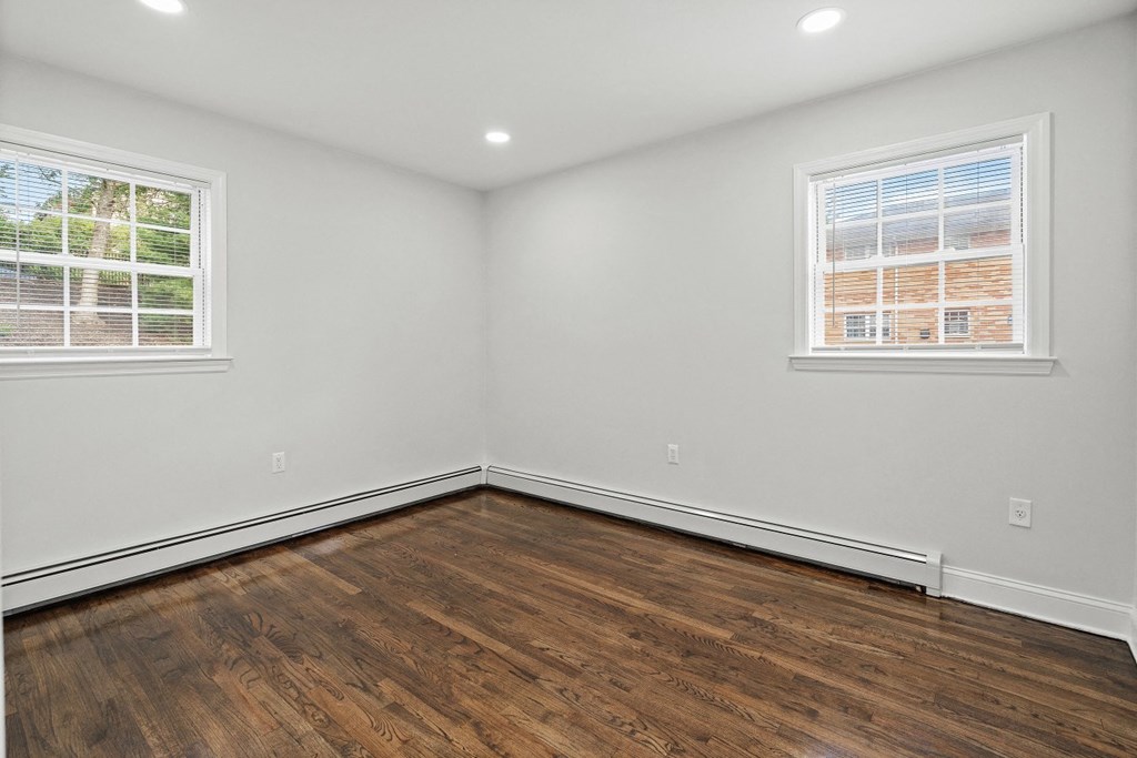 an empty bedroom with wood floors and two windows