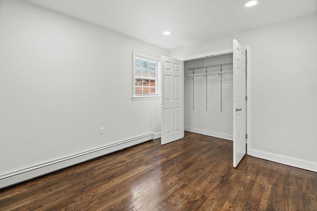 a bedroom with white walls and wood flooring and a closet