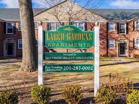 A sign for Larch Gardens Apartments sits in front of a brick building.