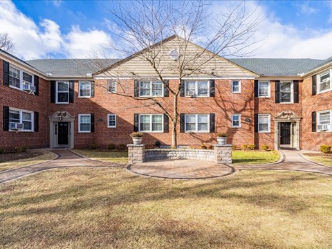 A large brick building with a tree in front and a circular walkway in the front yard.