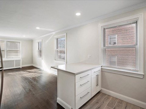 A kitchen with white cabinets and a window with blinds.