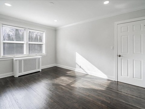 A room with a white door, window with blinds, and a radiator on the window.