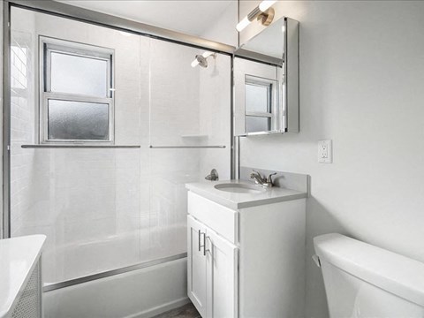 A white bathroom with a sink, mirror, and bathtub.