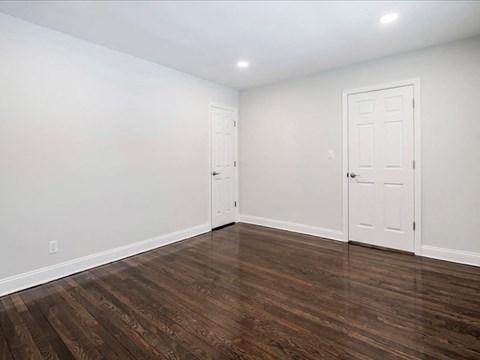 A room with white walls and wood flooring with two doors.