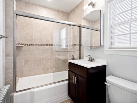 A bathroom with a white tub, sink, and a brown cabinet.