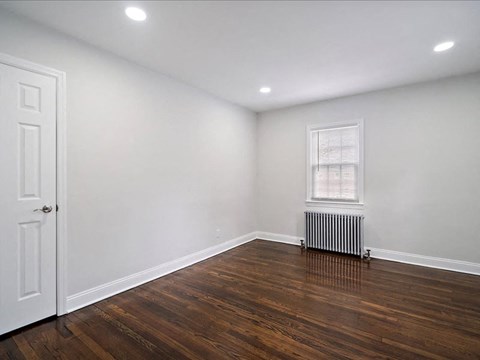 A room with a white door and a window with a radiator underneath it.