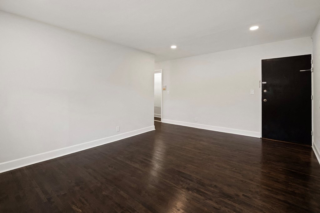 a living room with white walls and wood flooring and a black door