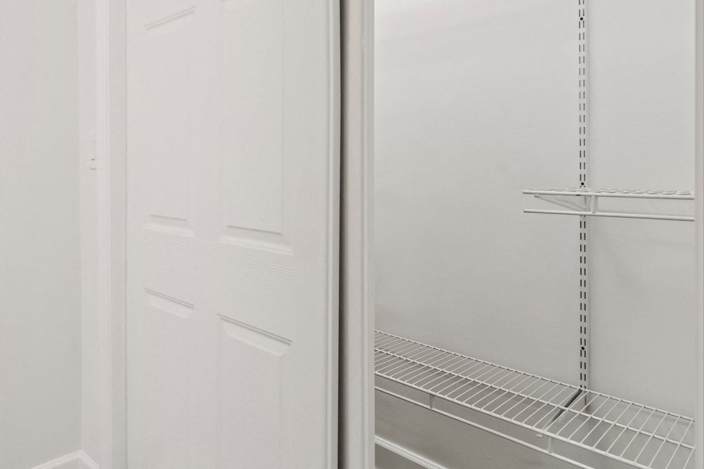 the closet has a white door and a white wall with a shelf in it