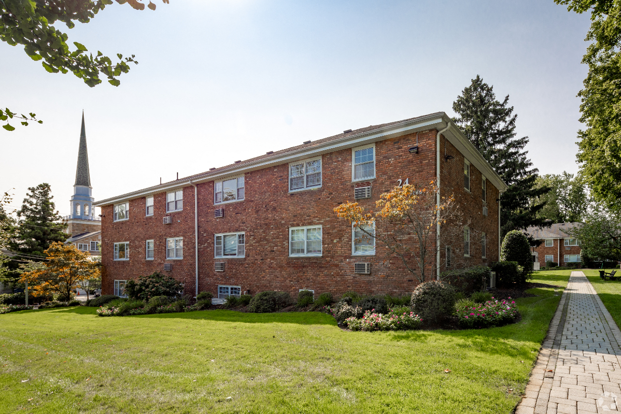 a brick building with a green lawn and a church in the background
