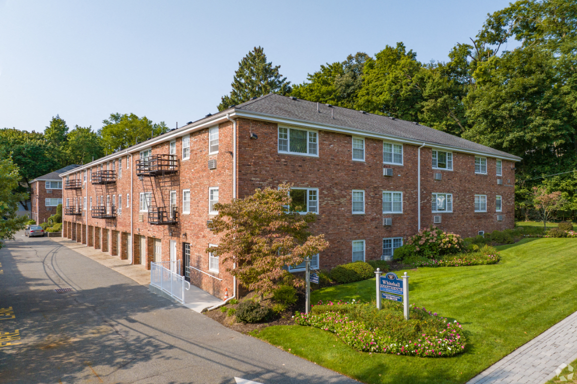 a red brick apartment building with a green lawn and a sidewalk