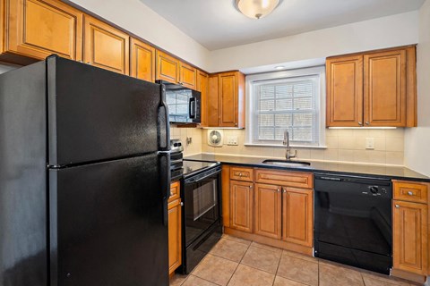 A black refrigerator is in a kitchen with wooden cabinets.