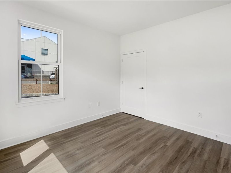 A room with a white door and a window showing a blue building outside.