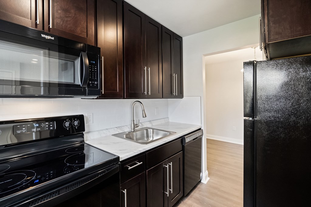 an empty kitchen with black appliances and dark wood cabinets