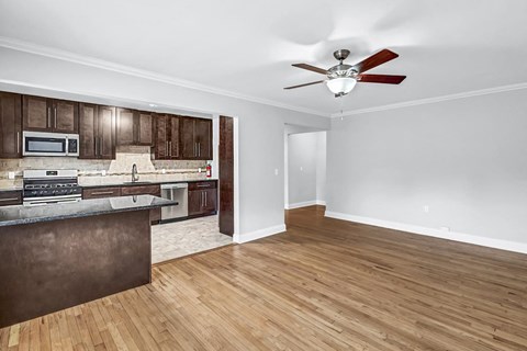 an empty living room with a kitchen and a ceiling fan