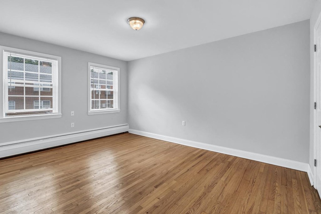 the living room of an empty home with wood flooring and two windows