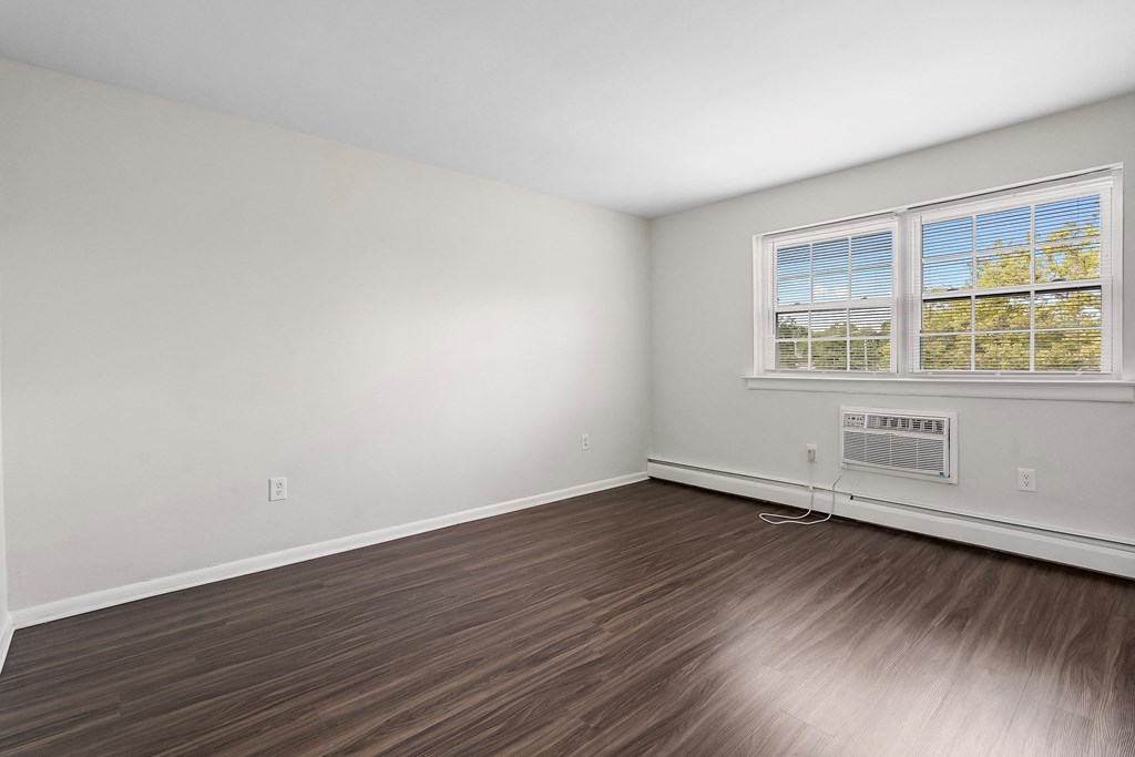the living room of an empty home with wood flooring and a window