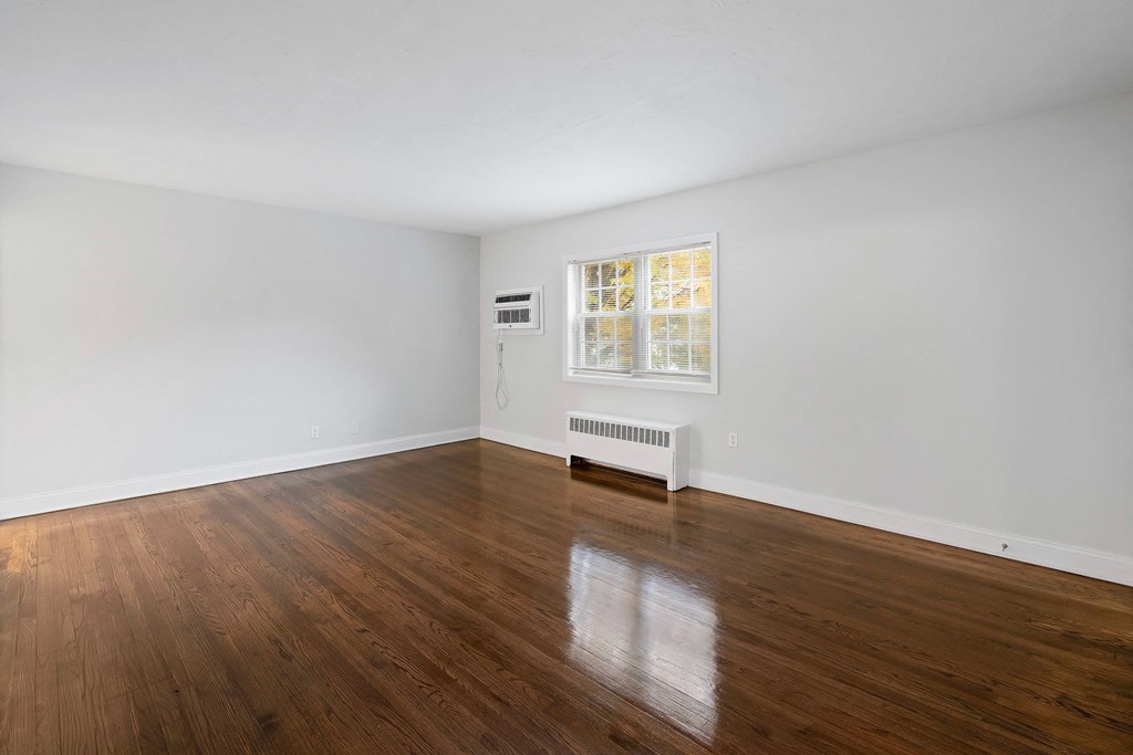 a living room with white walls and wood floors and a window