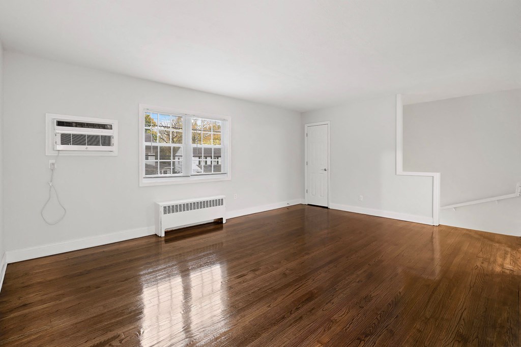 a living room with white walls and wood floors and a window