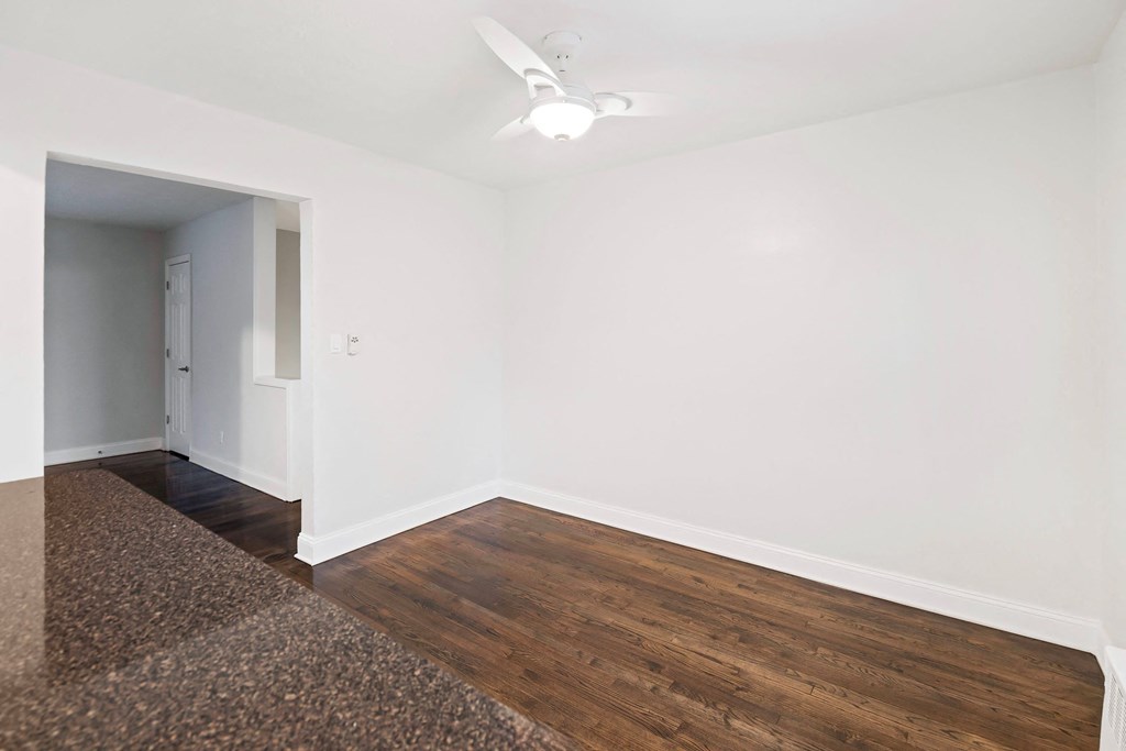 a living room with white walls and wood flooring and a ceiling fan