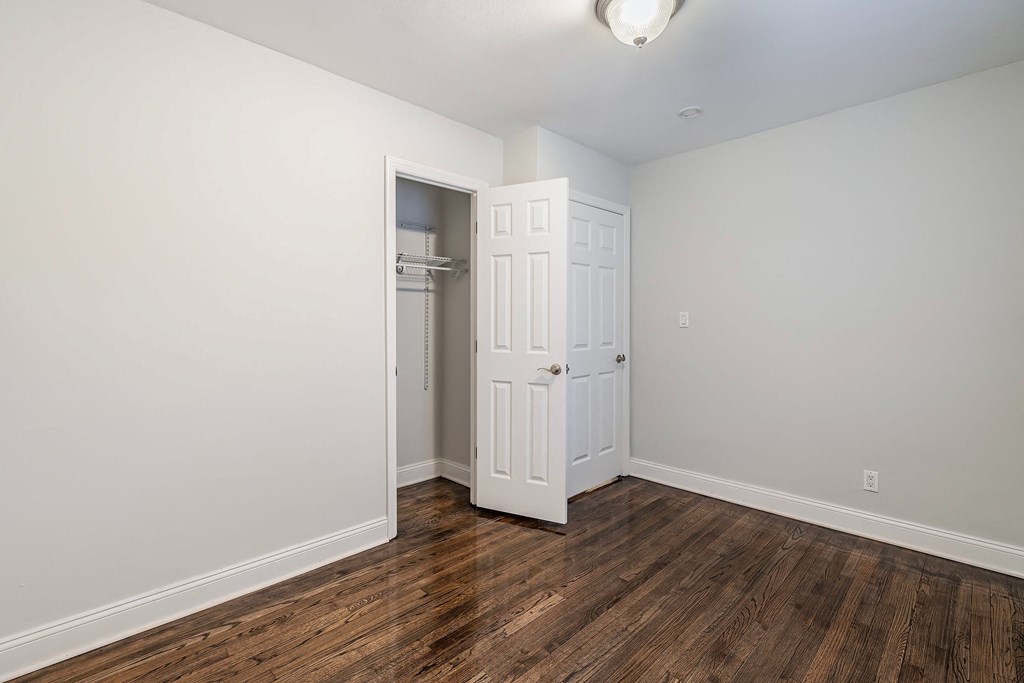 a bedroom with white walls and wood flooring and an open closet