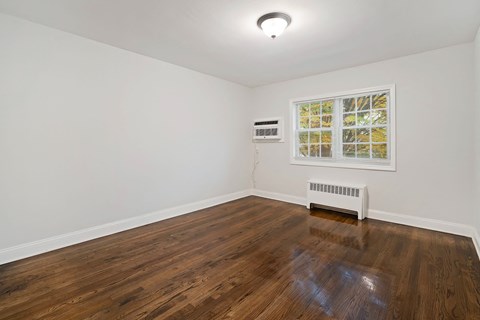 a living room with white walls and wood floors and a window