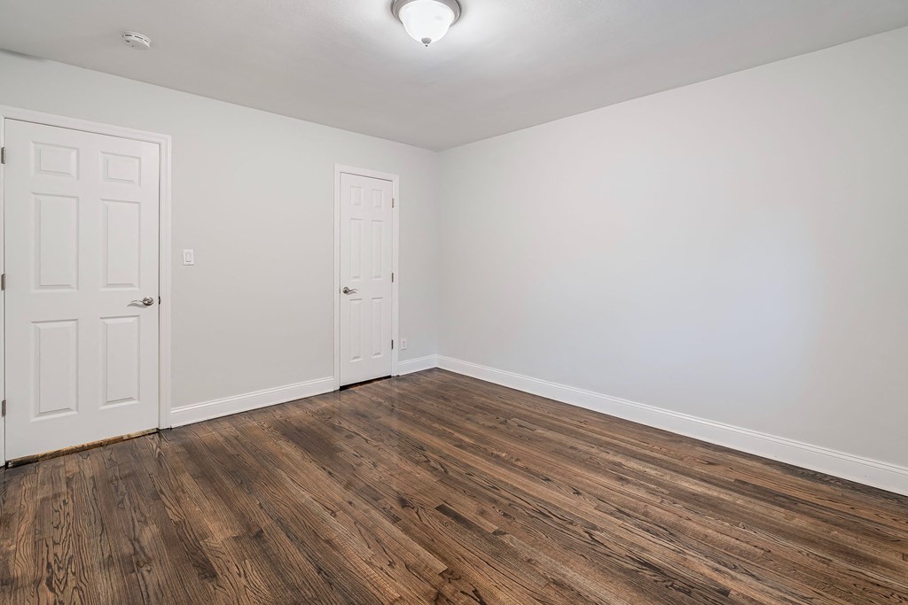 a bedroom with white walls and wood flooring and a door