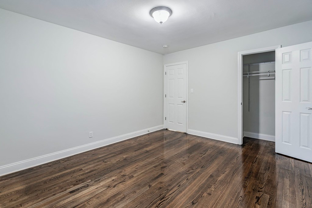 a bedroom with white walls and wood flooring and a closet