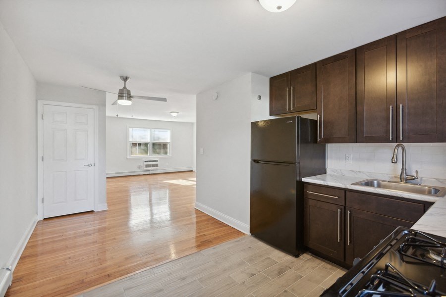an empty kitchen and living room with wood flooring and a stainless steel refrigerator