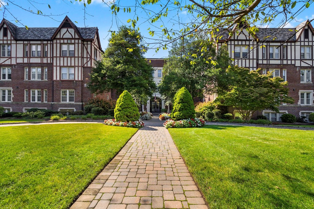 a brick walkway leading to a building with a lawn and trees