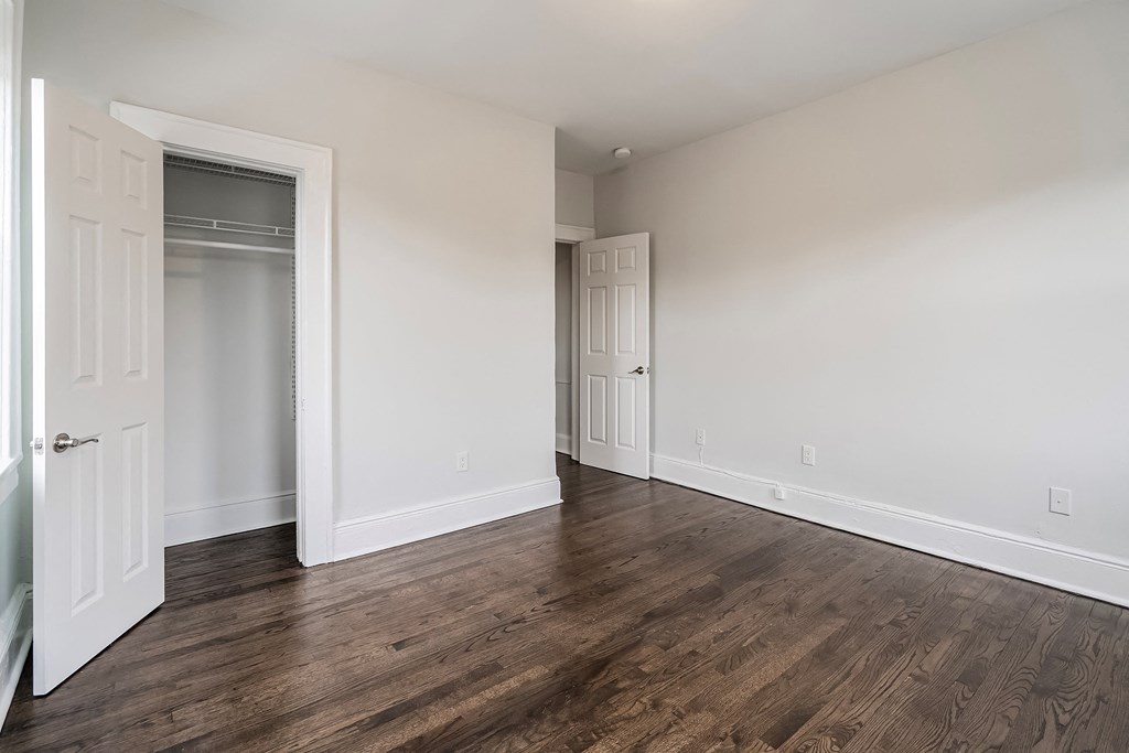 a bedroom with white walls and wood flooring and a closet