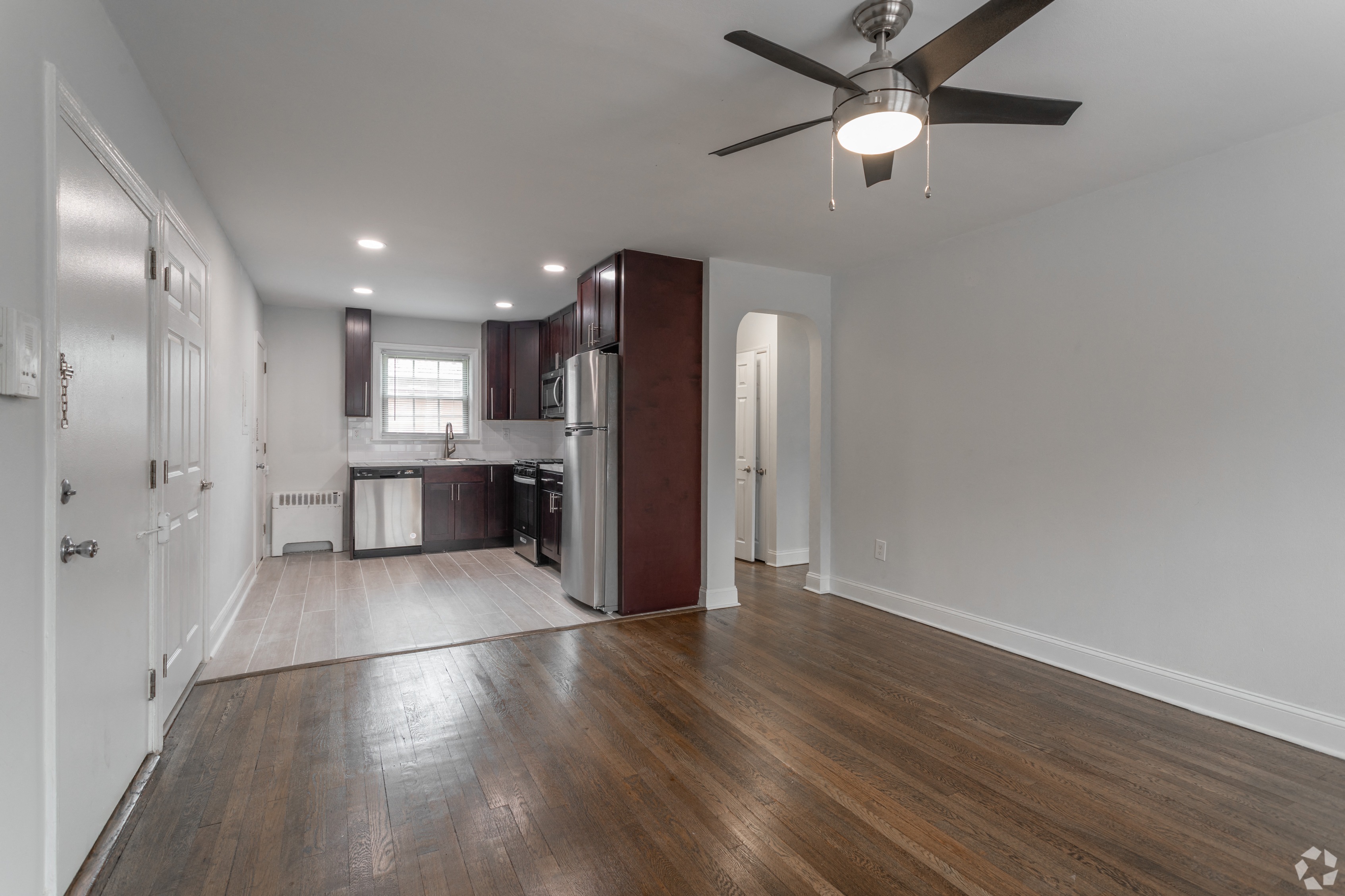 an empty living room and kitchen with wood floors and a ceiling fan