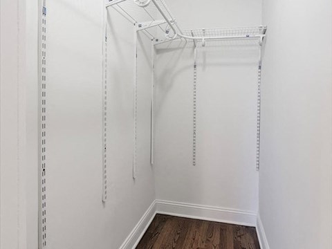 a walk in closet with white walls and a wood floor