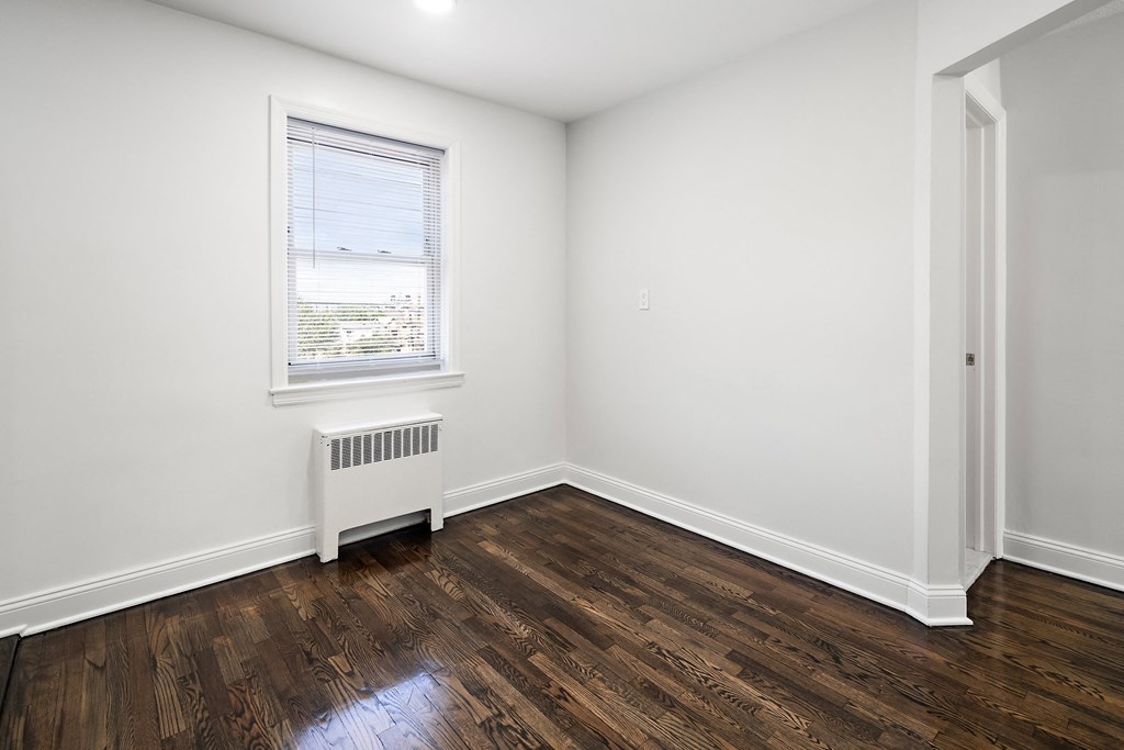 a bedroom with white walls and wood flooring and a window