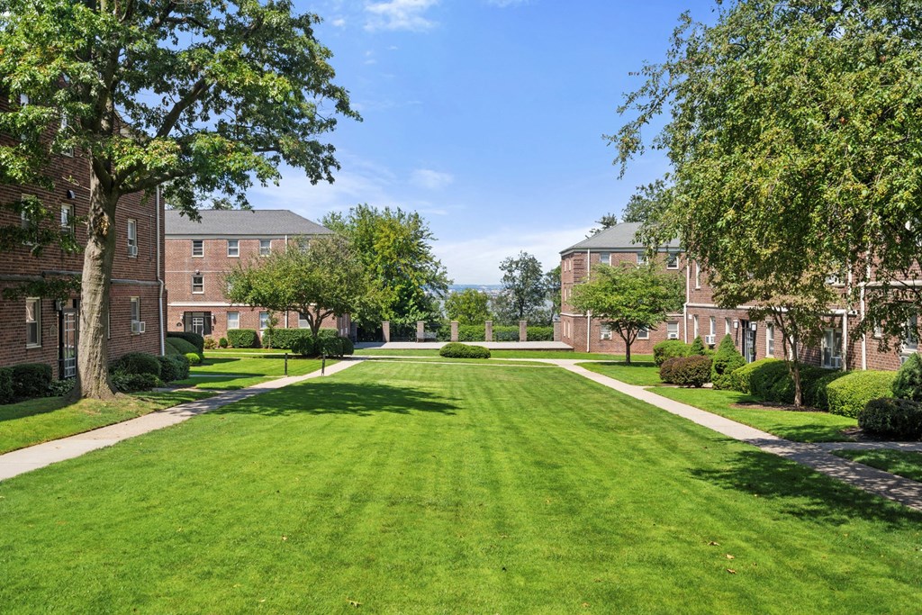 a green lawn in front of a brick building with trees