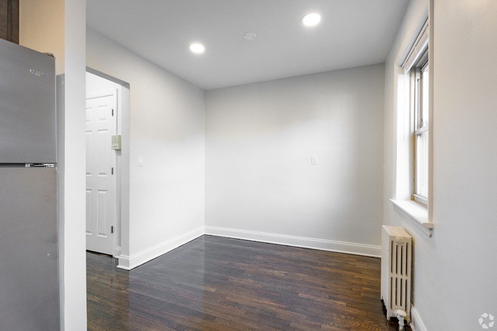 an empty room with white walls and wood flooring and a refrigerator
