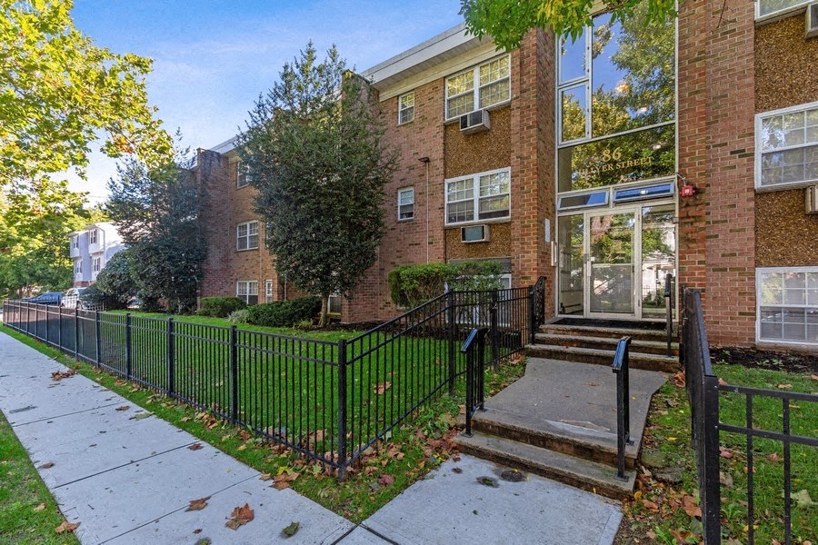 an apartment building with a sidewalk and a fence in front of it