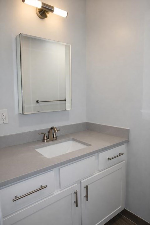 A bathroom with a sink, mirror and cabinets.