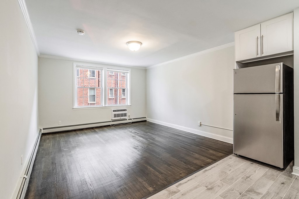 an empty living room with a refrigerator and a window