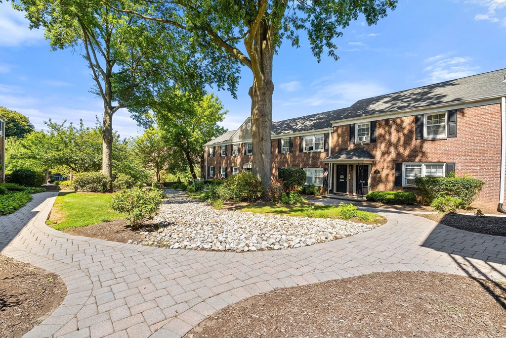 the front yard of a brick house with a cobblestone walkway and trees