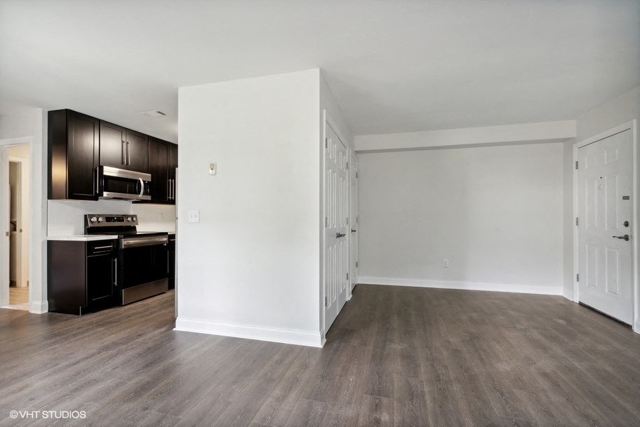 an empty living room and kitchen with wood floors and white walls