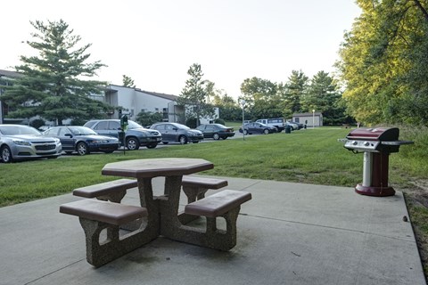 a picnic table with benches and a grill on a sidewalk