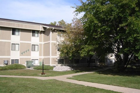 an apartment building with a sidewalk and trees in front of it