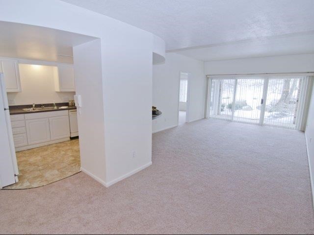 an empty living room with a kitchen and a window