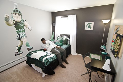 a man sitting on a bed in a room with a green and white bedspread