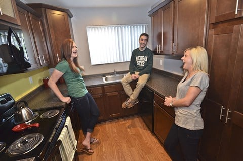 three people in a kitchen with a stove and a sink