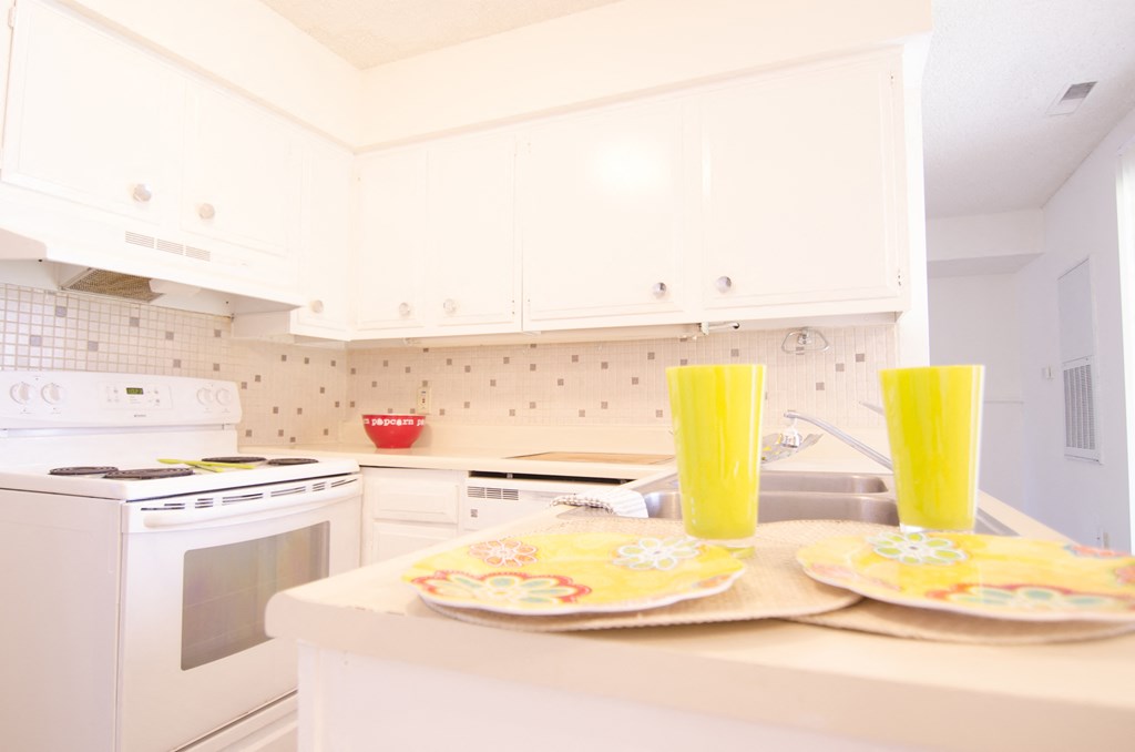 a white kitchen with yellow glasses on the counter