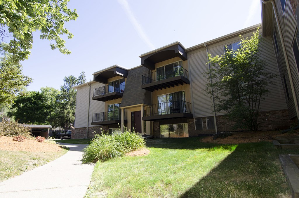 the exterior of an apartment building with a sidewalk and grass