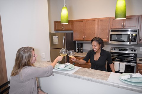 two women sitting at a kitchen counter drinking wine